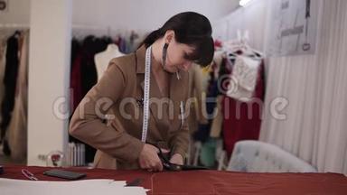 女时装设计师穿着时髦的西装和耳环，在充满剪裁工具的工作室里用<strong>红色布</strong>料工作-
